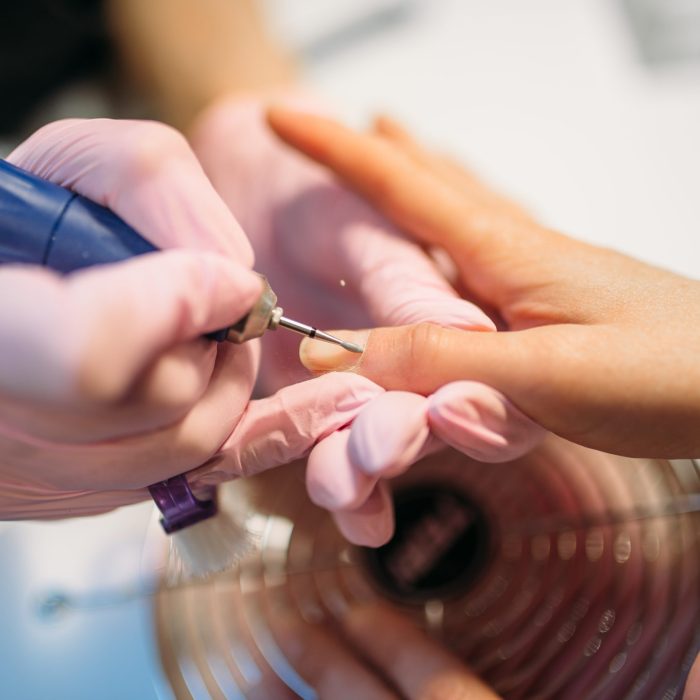 Beautician in gloves polishing nails of female client, top view, manicure in beauty salon. Manicurist doing hands care cosmetic procedure